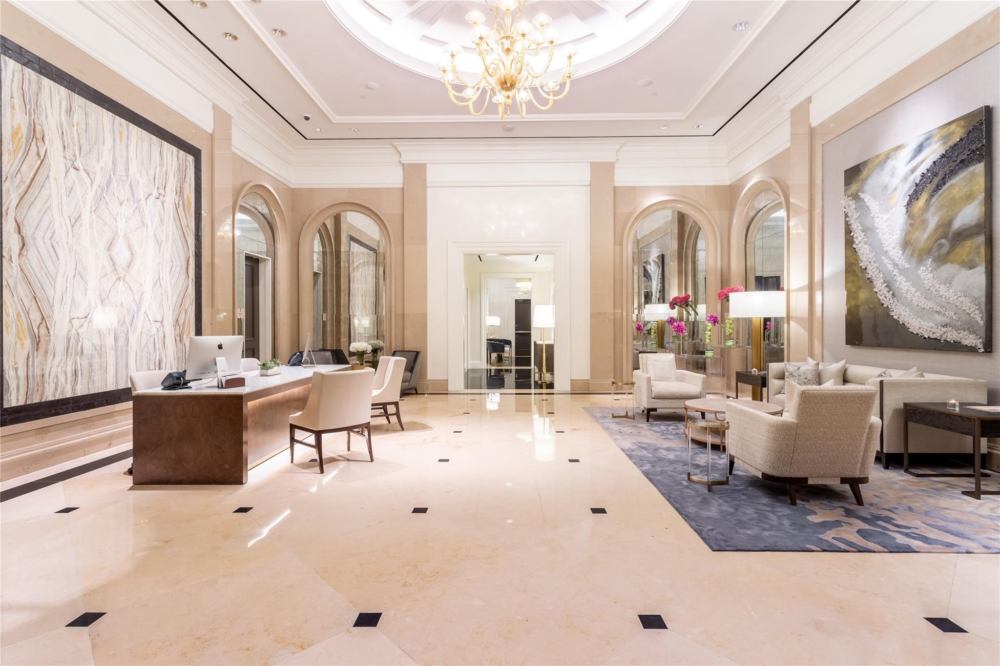 High-rise lobby with a marble reception desk, chandelier, arched mirrors, and lounge seating.