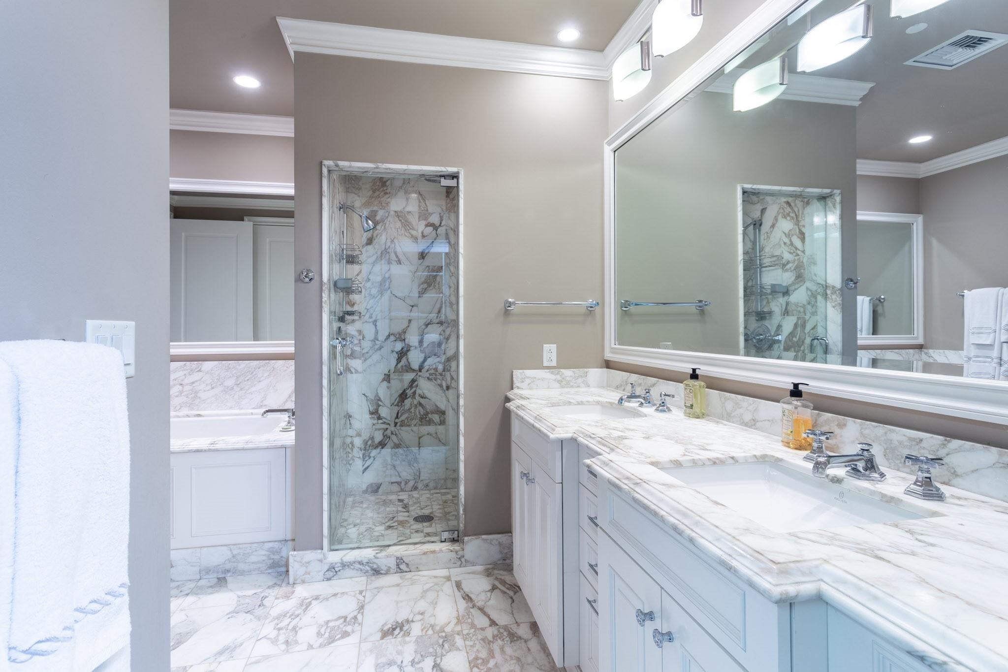 Bathroom with a marble double vanity, glass-enclosed shower, and bathtub.