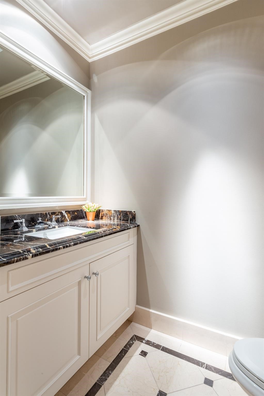 Bathroom vanity with dark veined marble counter, cream cabinetry, and geometric marble flooring.