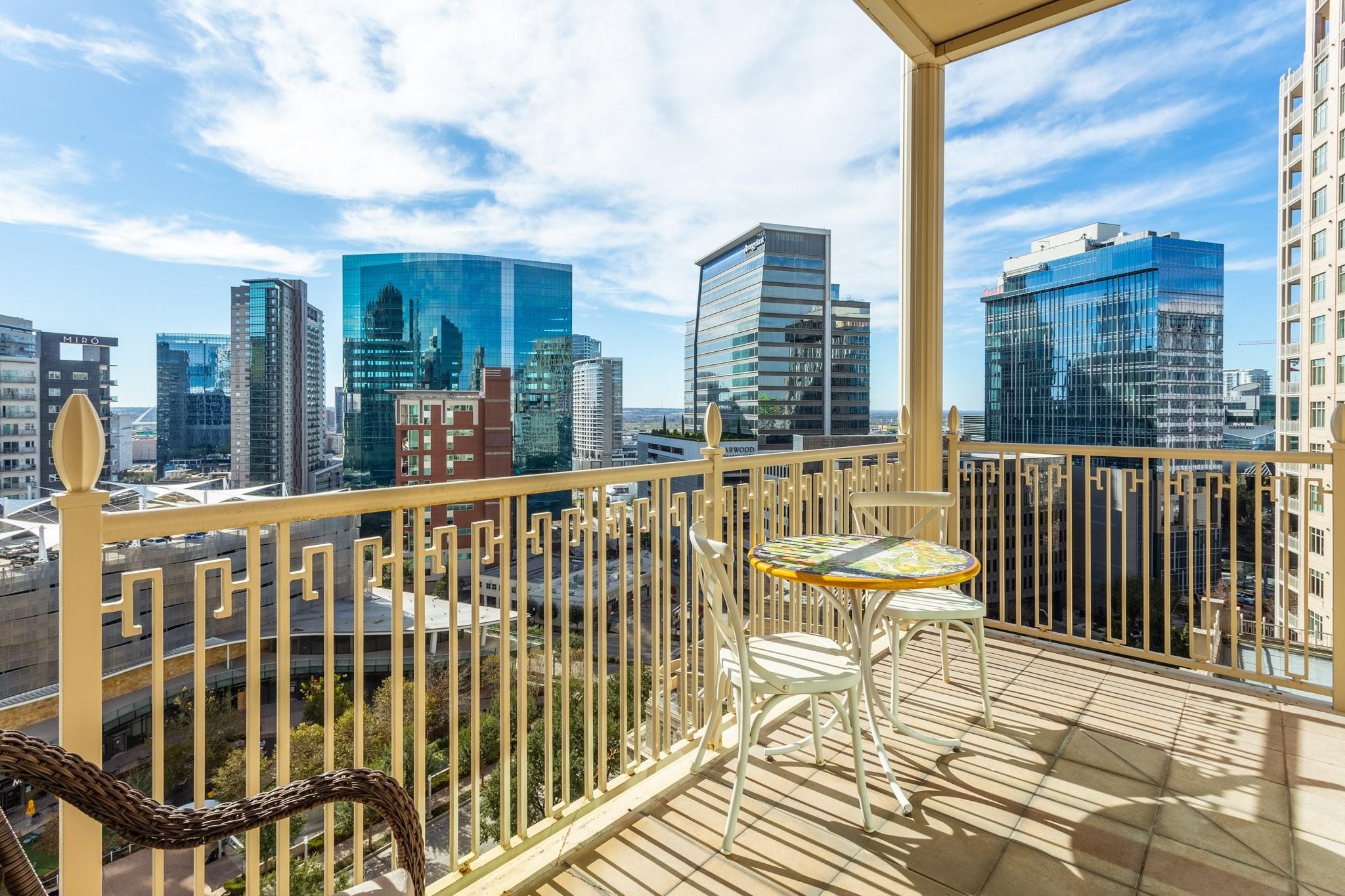 High-rise balcony with a small dining set overlooking downtown Dallas skyscrapers.