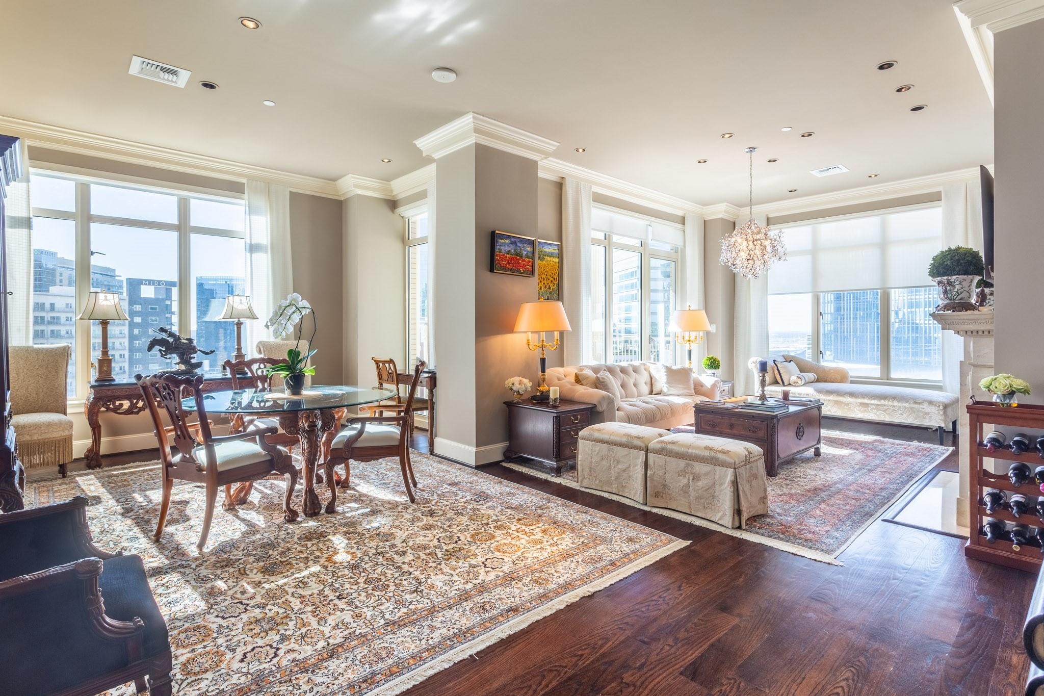 Furnished condo living and dining room with floor-to-ceiling windows overlooking downtown buildings.