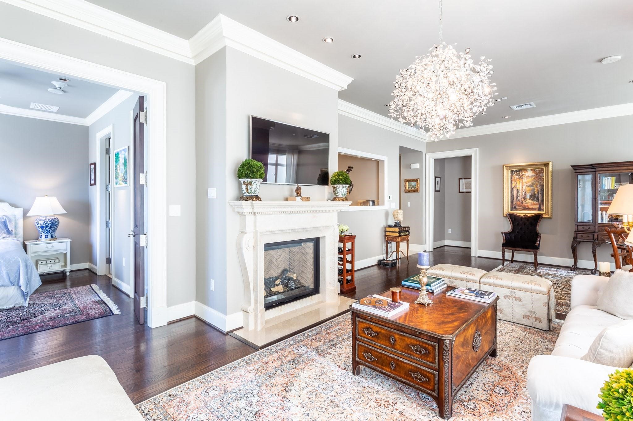 Furnished living room with a white fireplace, crystal chandelier, and adjoining bedroom.