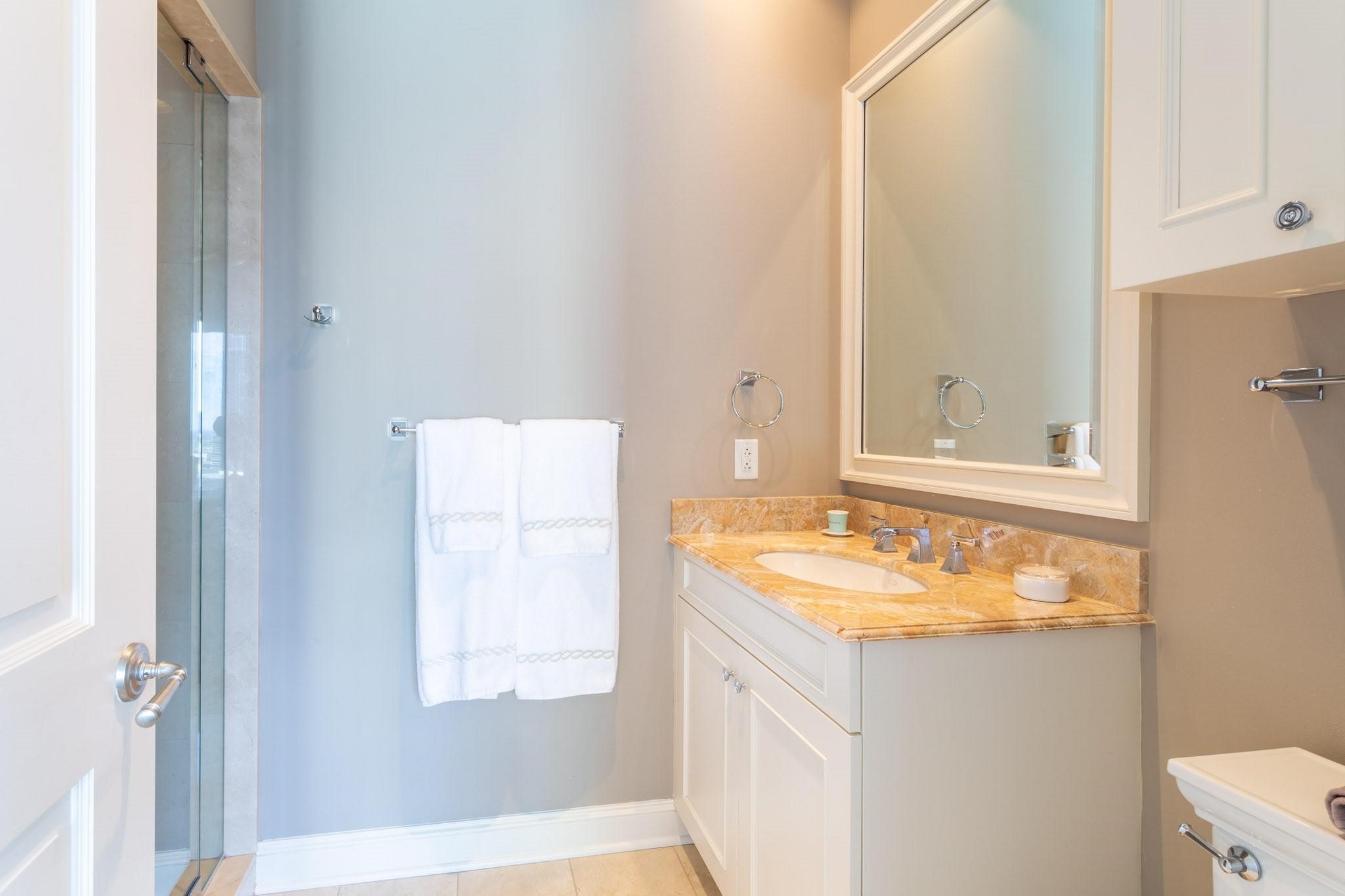 Bathroom with a glass shower and white vanity topped with golden stone.