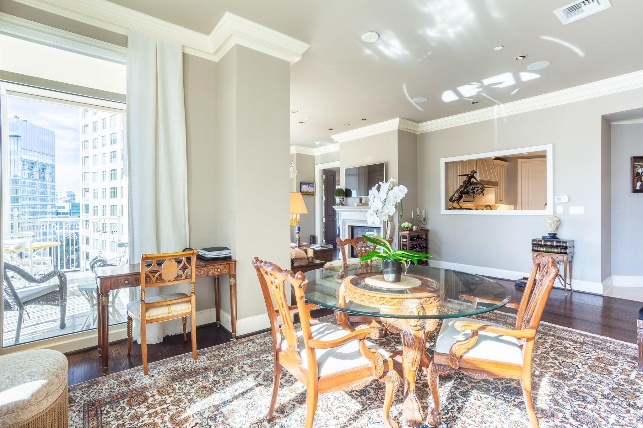 Furnished dining area with an ornate glass-top table and city skyline views through floor-to-ceiling windows.