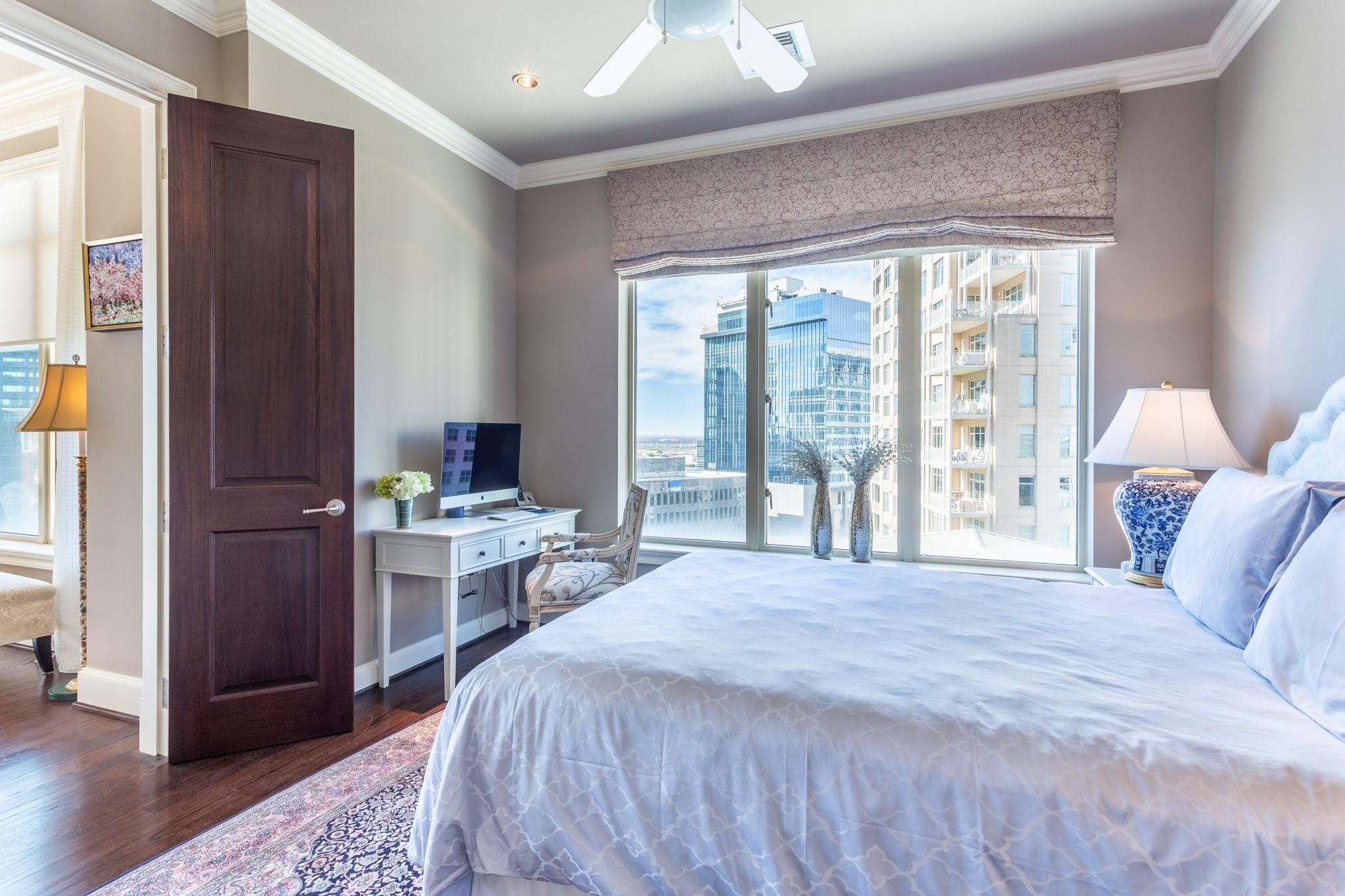 Furnished high-rise bedroom with a large bed, desk, and city views through floor-to-ceiling windows.