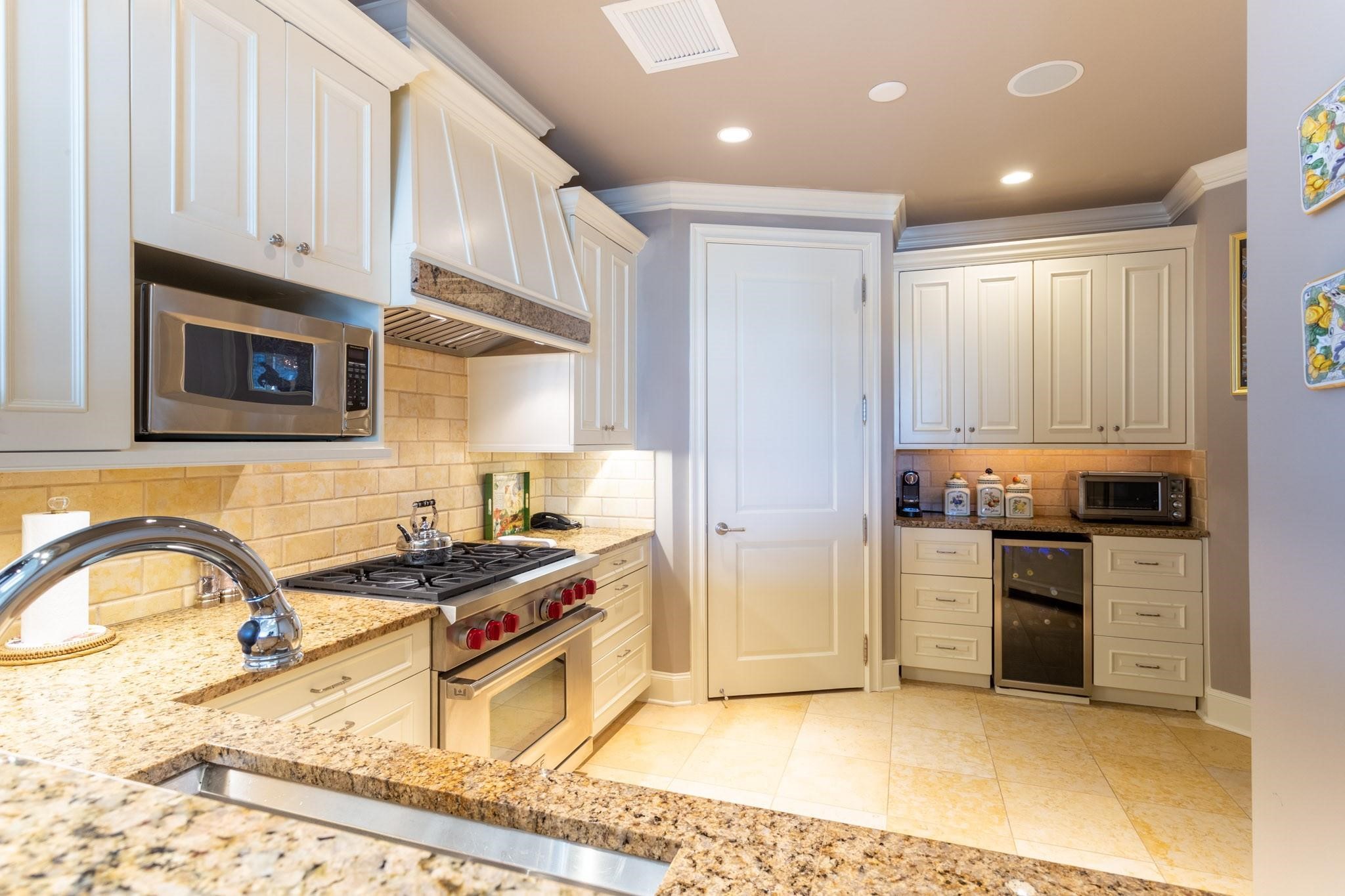 Kitchen with cream cabinets, granite counters, gas range, tan tile backsplash, and a built-in wine refrigerator.