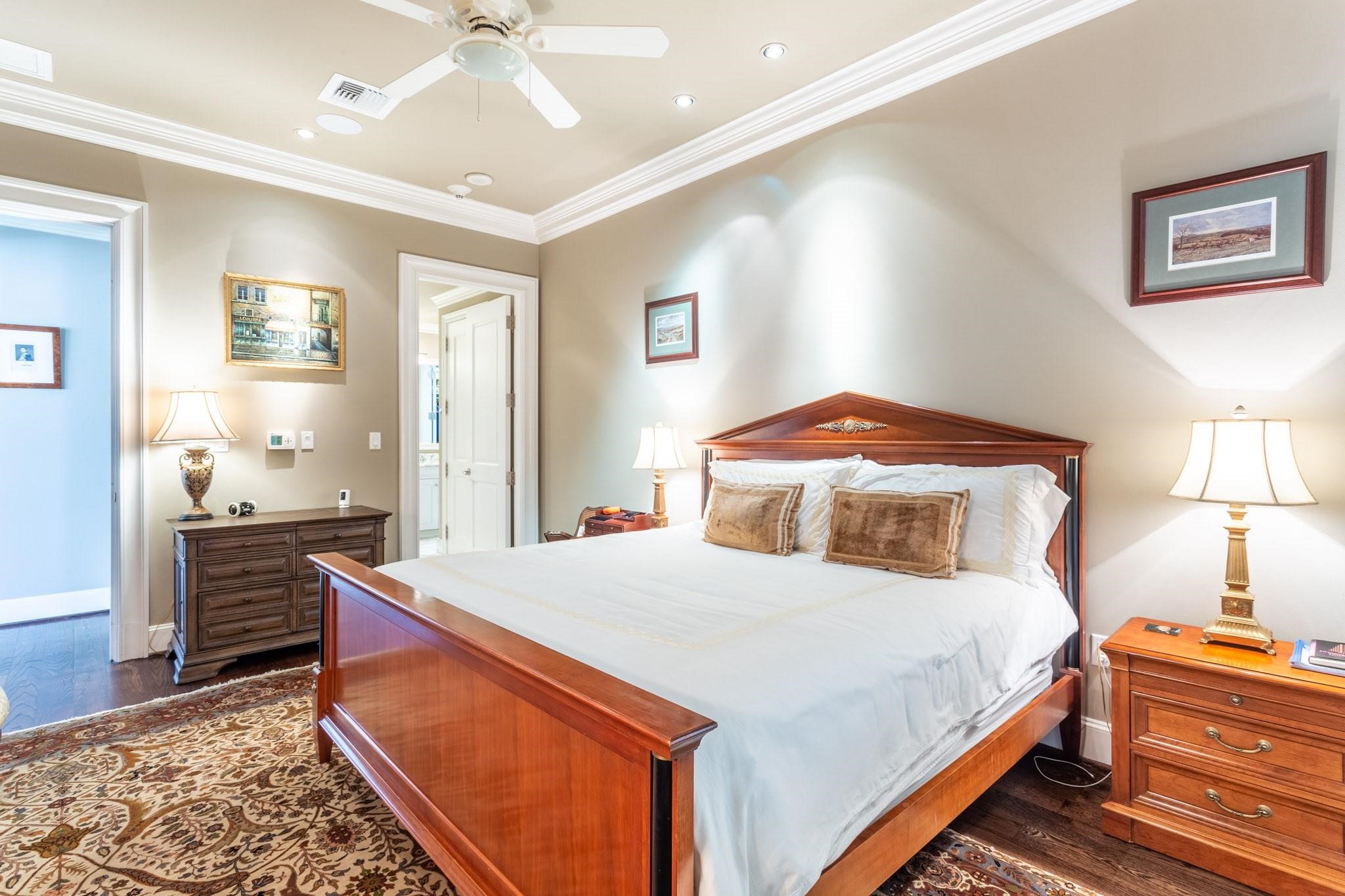 Furnished bedroom with a large wooden bed, white bedding, matching dressers, and a patterned rug.