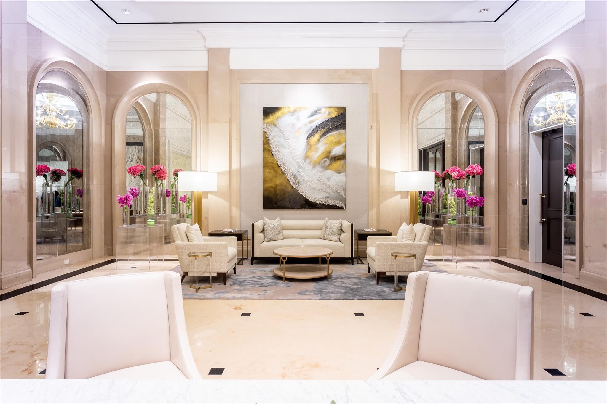 High-rise lobby with cream seating, arched mirrors, pink flowers, and a large abstract painting.