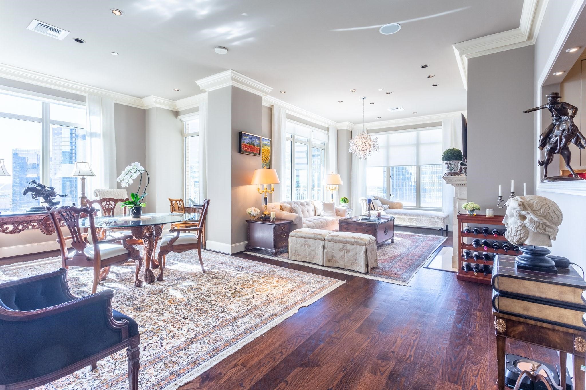 High-rise living and dining room with ornate wood furniture and city views through large windows.