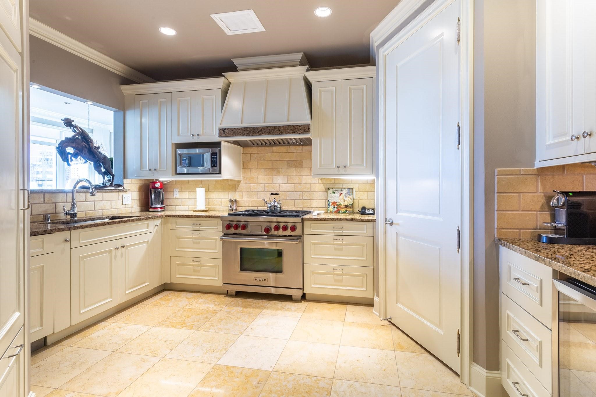 Kitchen with cream cabinets, granite counters, and a stainless range beneath a paneled hood.