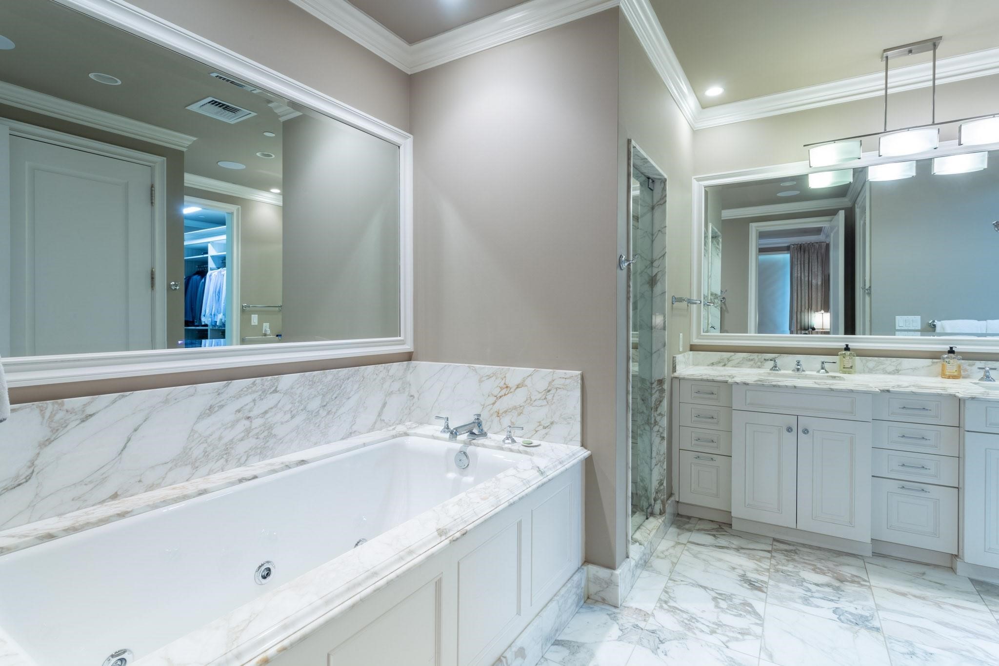 Bathroom with a marble-surrounded soaking tub, glass shower, and white double vanity.