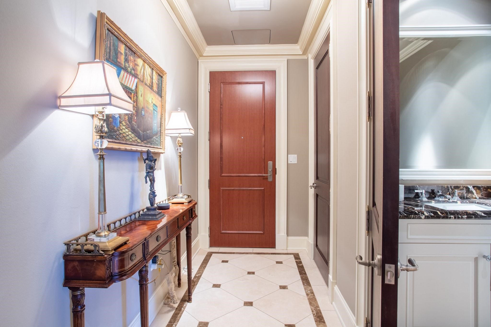 Condominium entry hall with a wood front door, patterned tile, and a console table beside an open bathroom doorway.