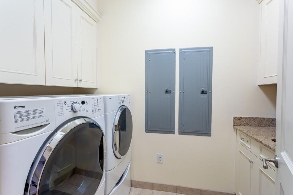 Laundry room with front-loading washer and dryer beside white cabinets and a granite countertop.