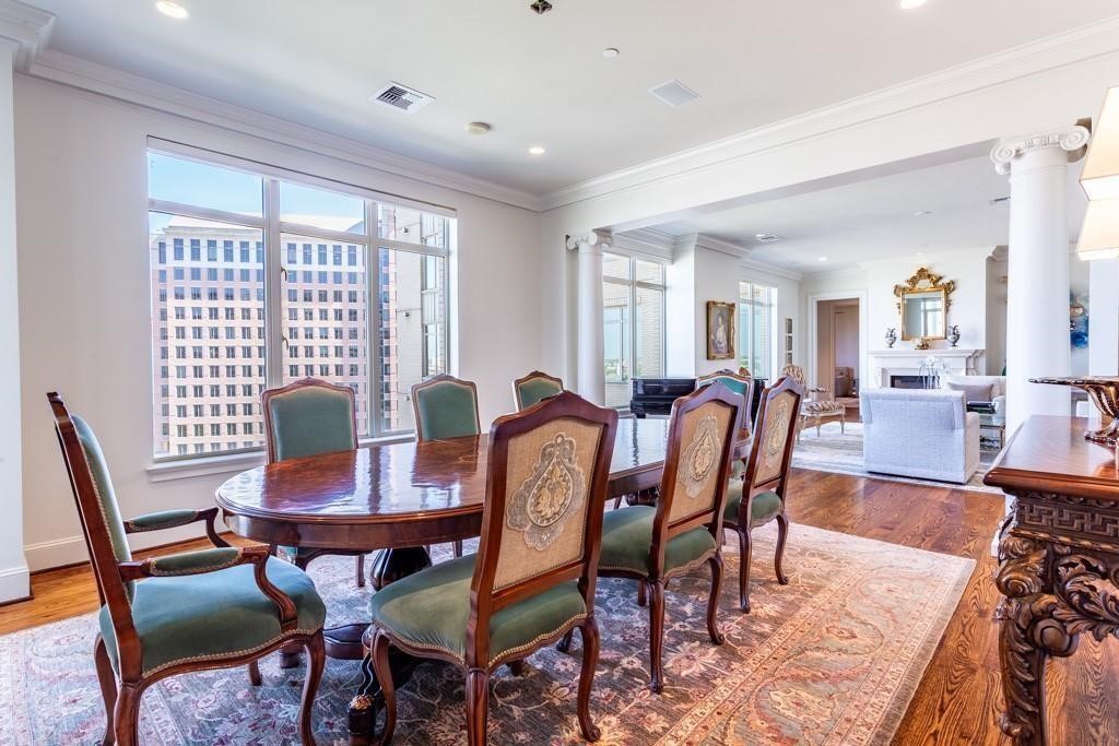 Formal dining room with an oval wood table, ornate chairs, and large windows overlooking city buildings.