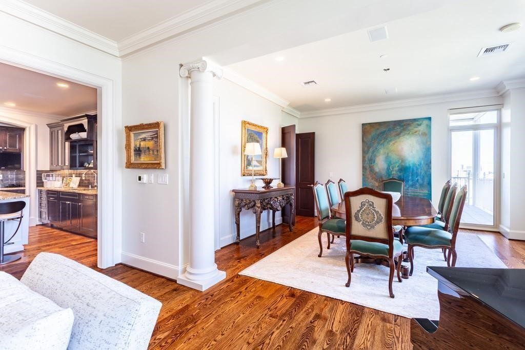 Dining room with a wooden table, upholstered chairs, hardwood floors, and a view into the kitchen.