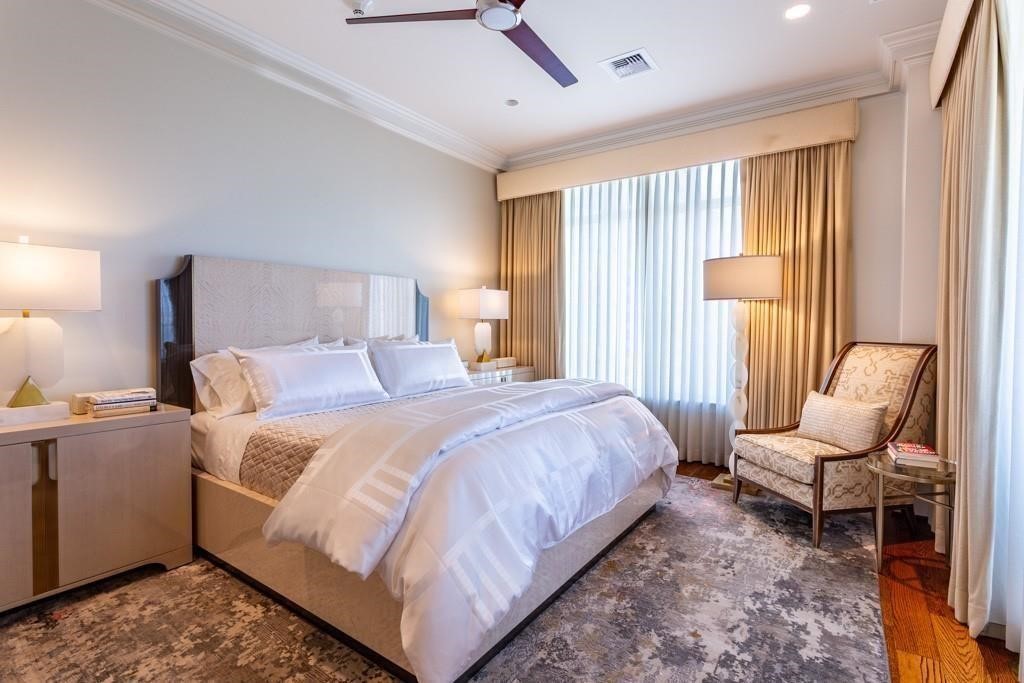 Furnished bedroom with a large bed, tall curtained windows, and an upholstered accent chair.