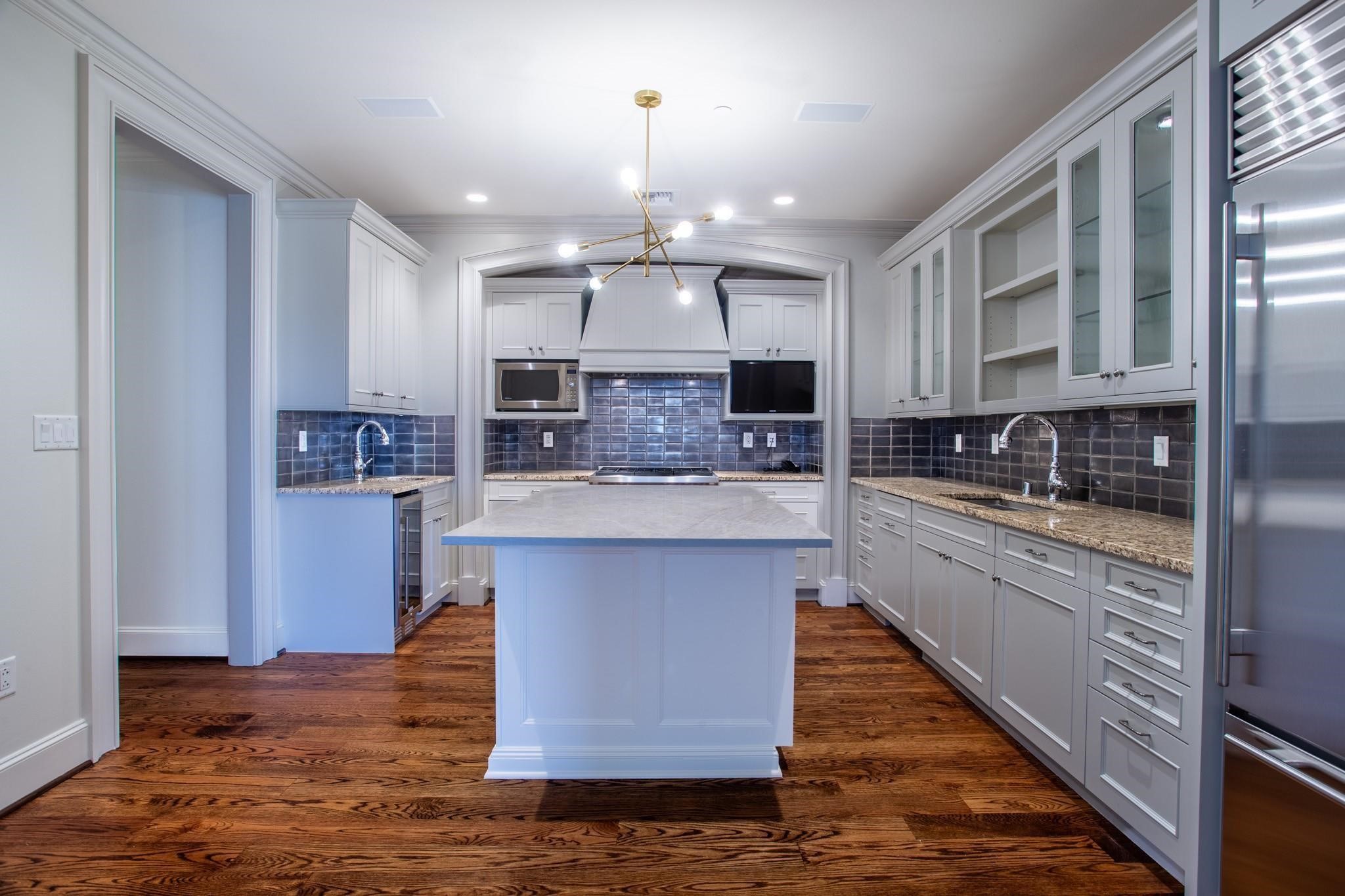 Kitchen with white cabinets, dark tiled backsplash, central island, stainless steel appliances, and hardwood floors.