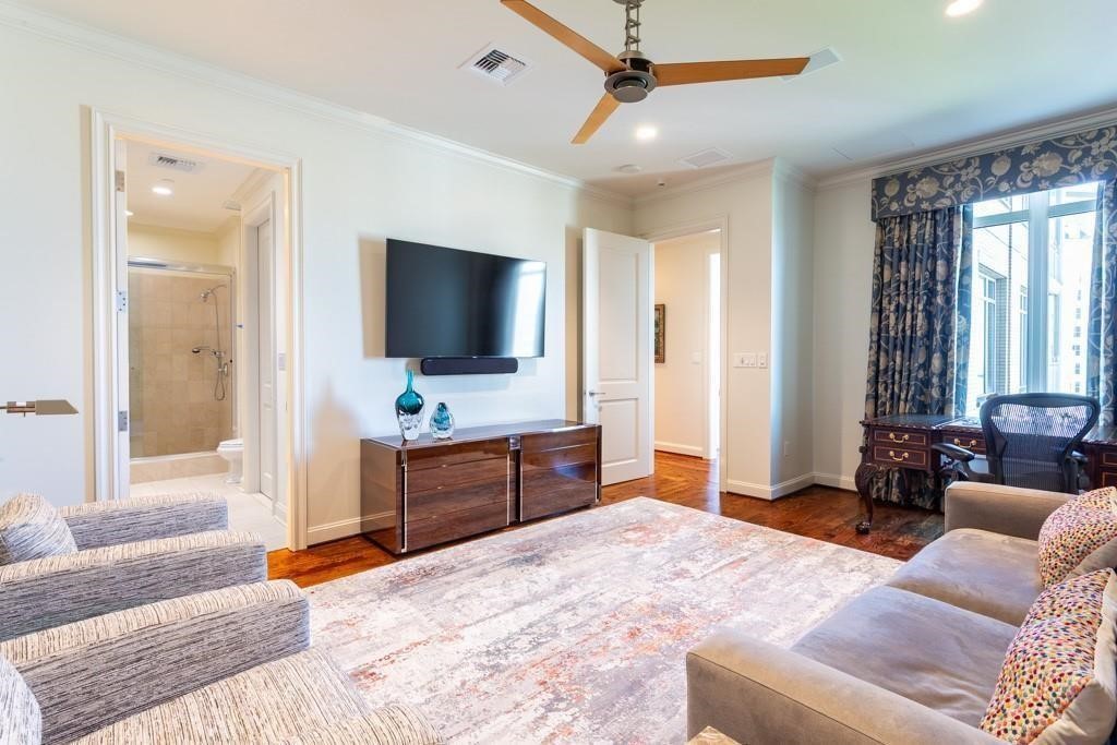 Furnished living room with hardwood floors, a ceiling fan, wall-mounted TV, and a desk by the windows.