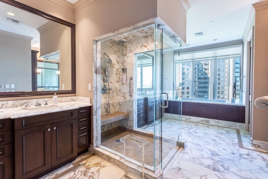Marble condo bathroom with a glass shower, dark wood vanity, and soaking tub overlooking downtown high-rises.