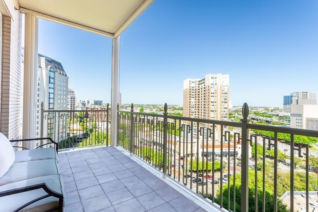 Covered high-rise balcony with tiled floor, seating, and a view of the Dallas skyline.
