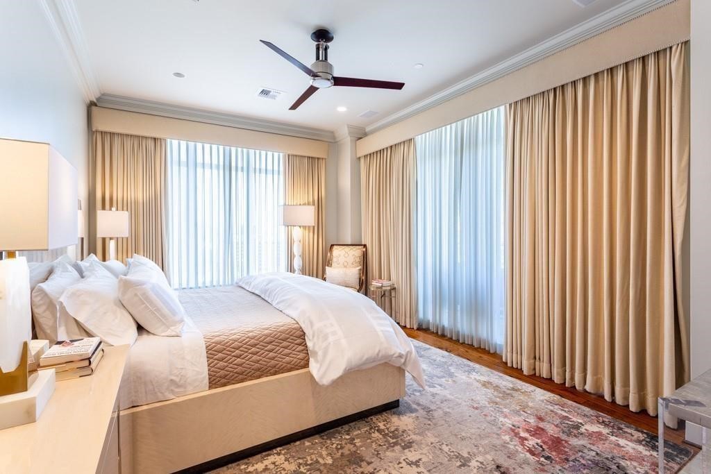 Furnished bedroom with a large bed, ceiling fan, and tall curtained windows.