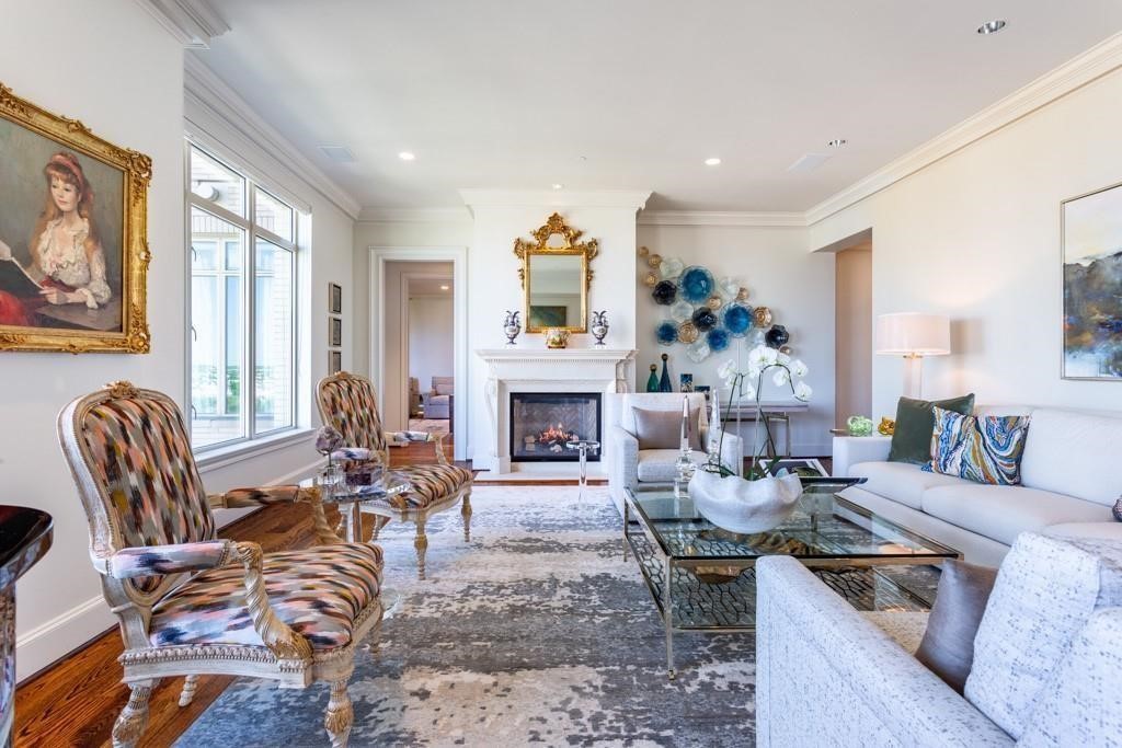 Furnished living room with a fireplace, tall windows, patterned chairs, and a white sofa.