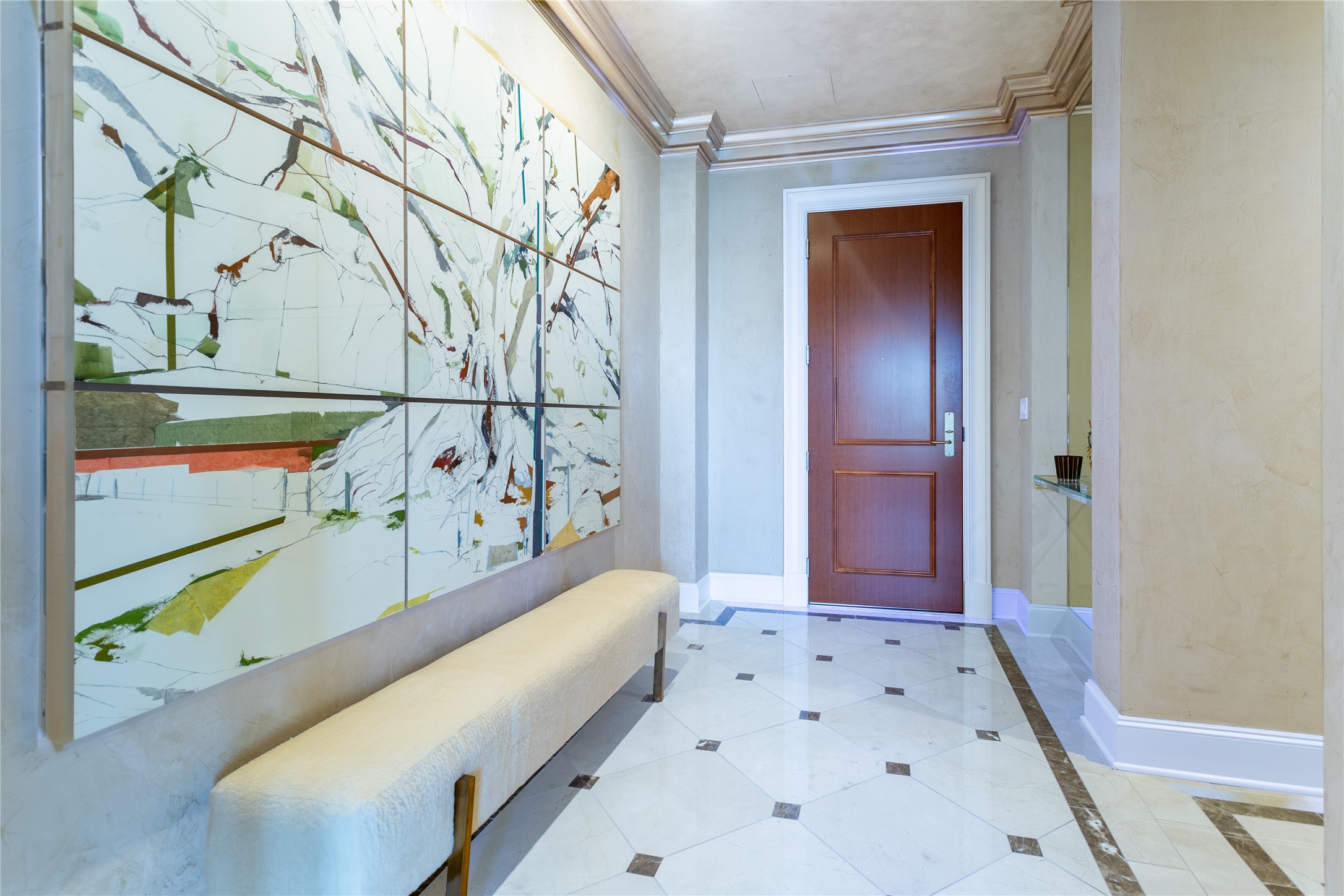 Condo entry foyer with a wood door, marble tile floor, cream bench, and large abstract wall art.