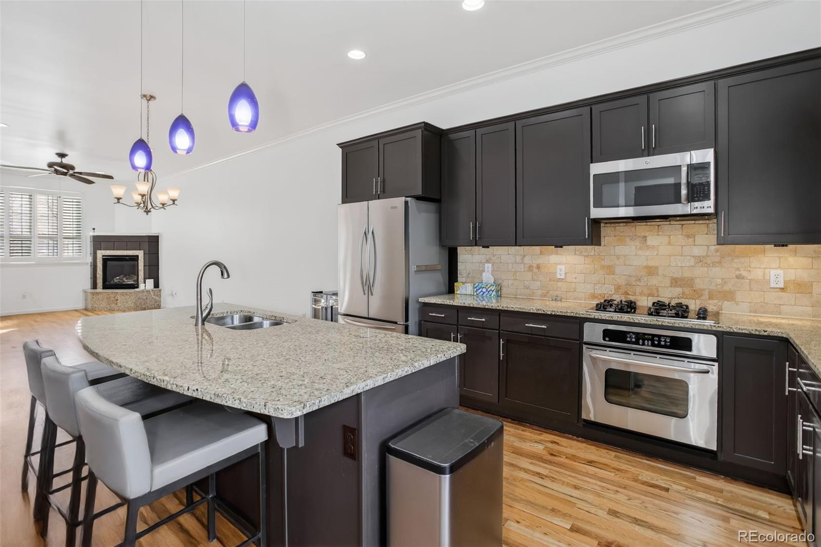 Kitchen with dark cabinets, stainless steel appliances, and a large granite island beside an adjoining living area.