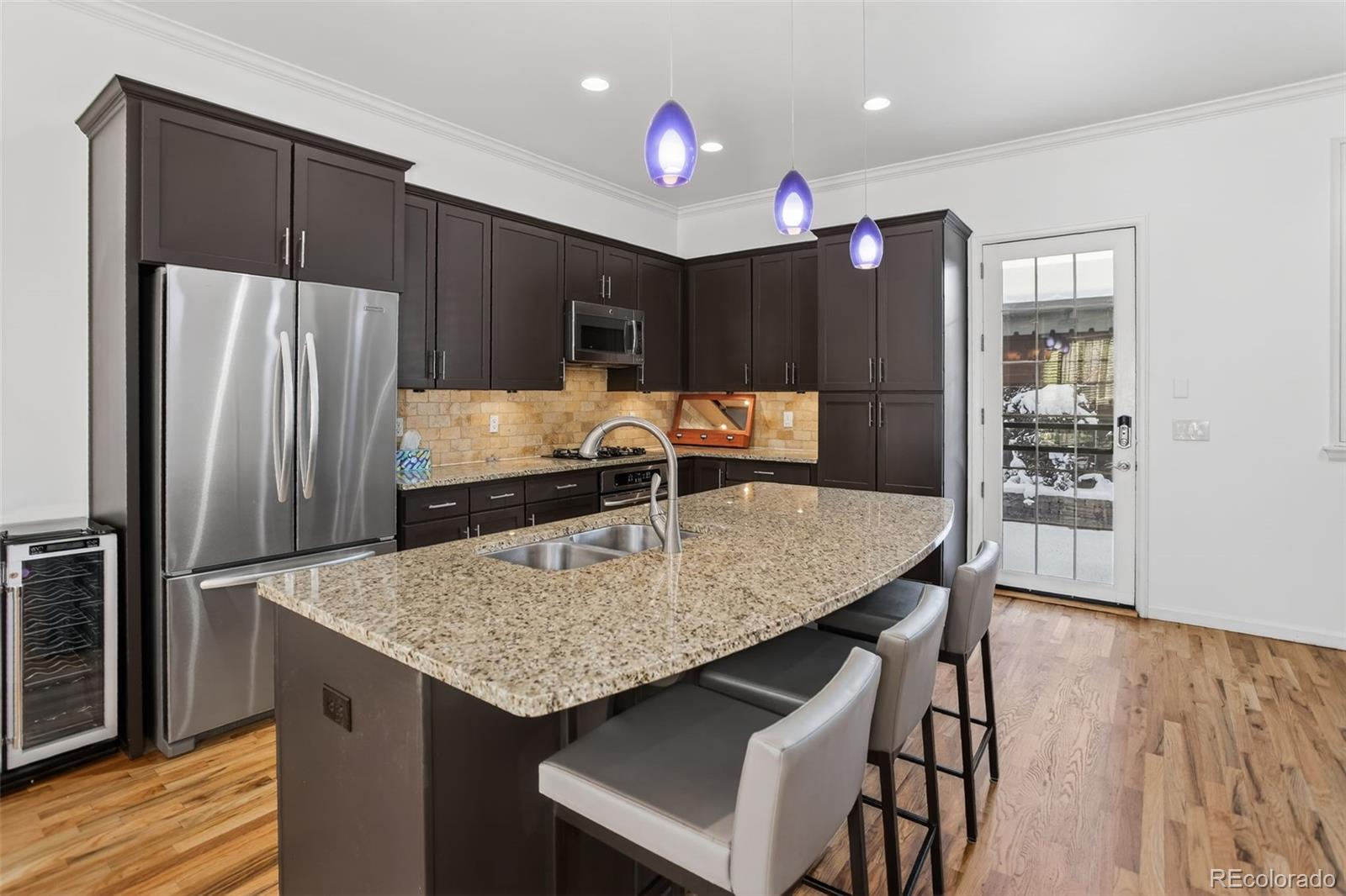Kitchen with dark cabinets, a granite island, stainless steel appliances, and three purple pendant lights.
