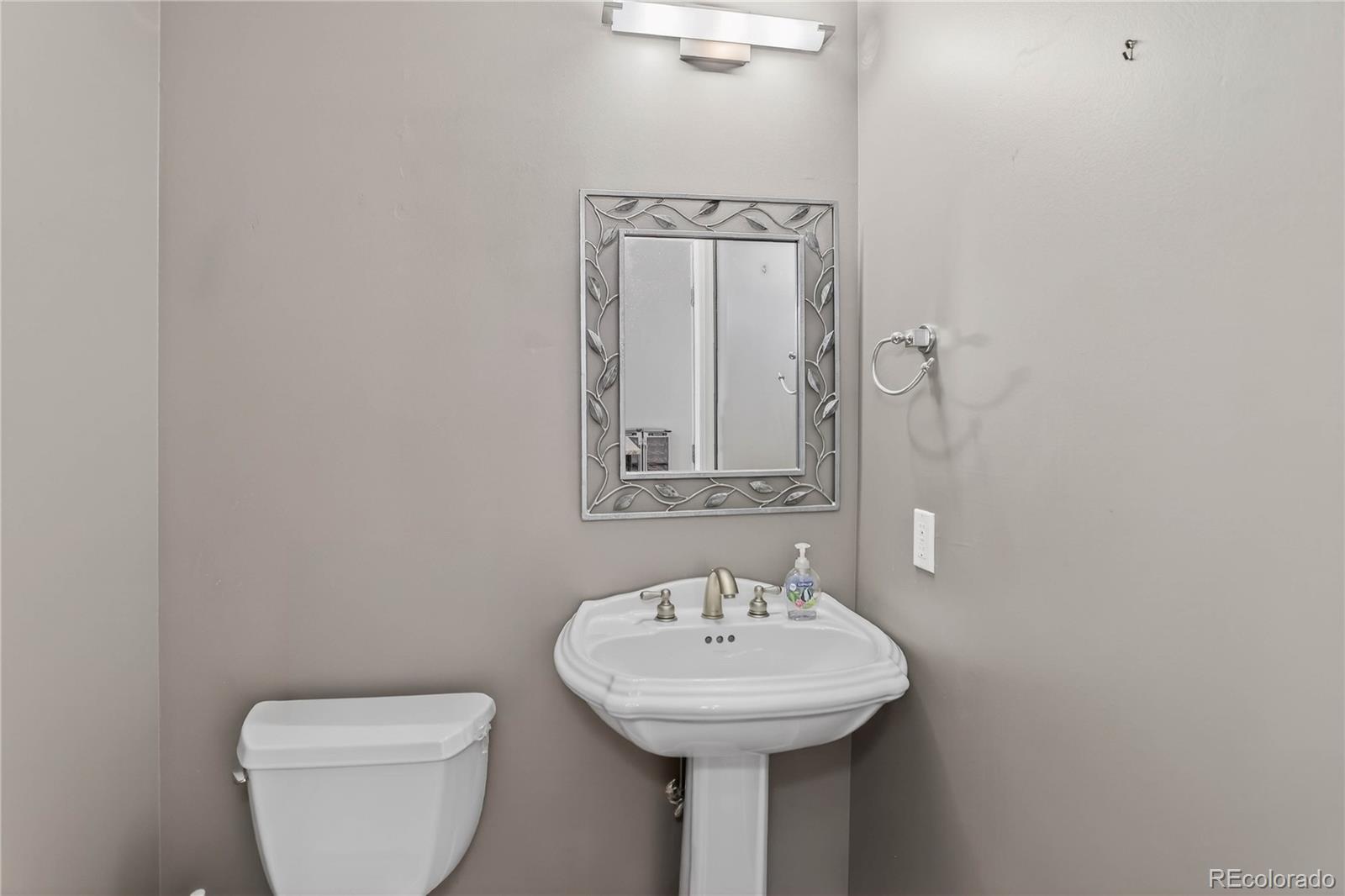 Bathroom with a white pedestal sink, toilet, and decorative framed mirror.