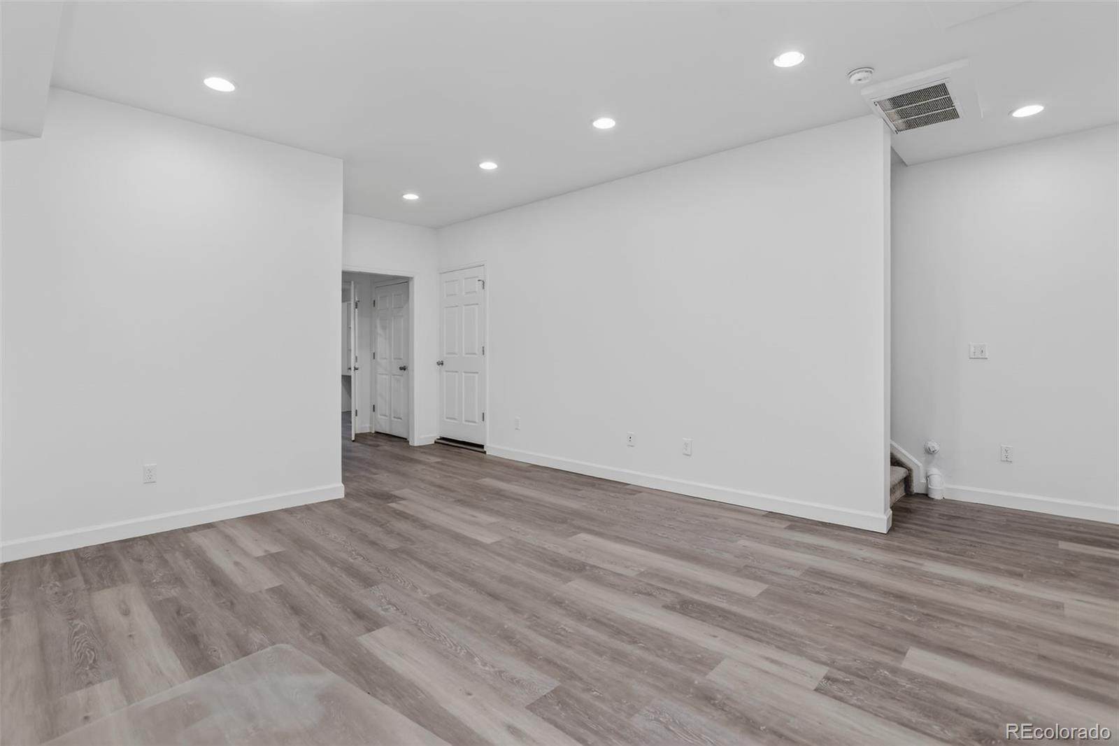 Vacant room with gray plank flooring, recessed lights, and a stairway opening.