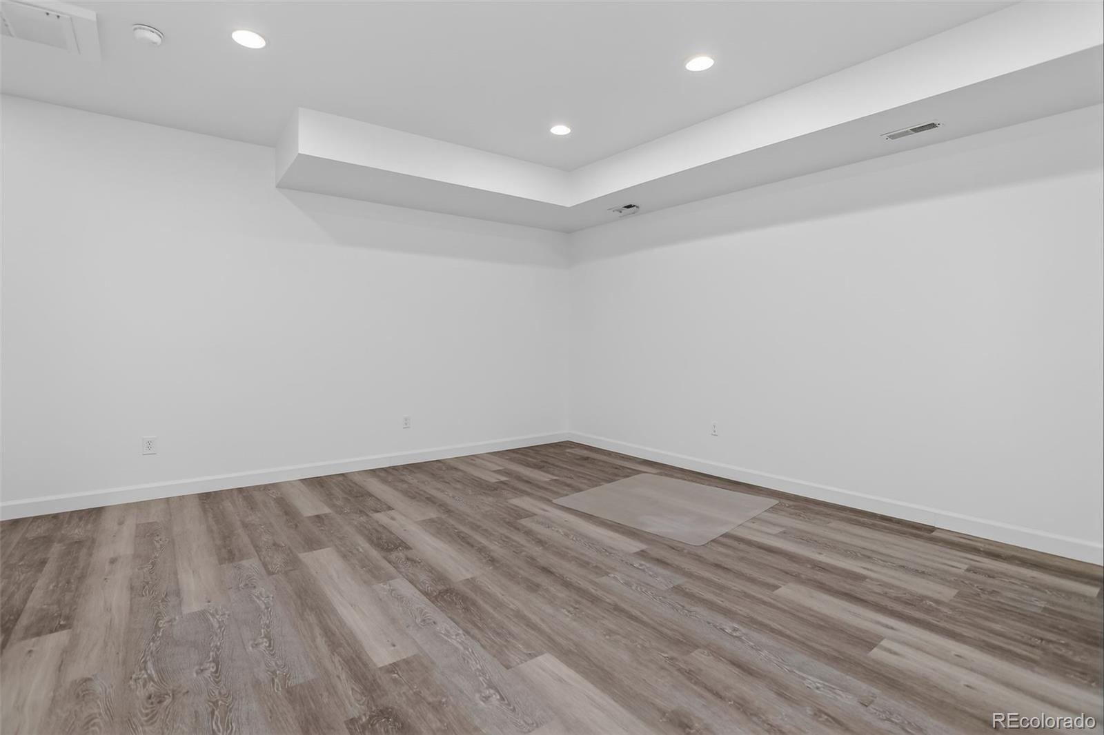 Empty interior room with gray wood-look flooring, white walls, and recessed ceiling lights.