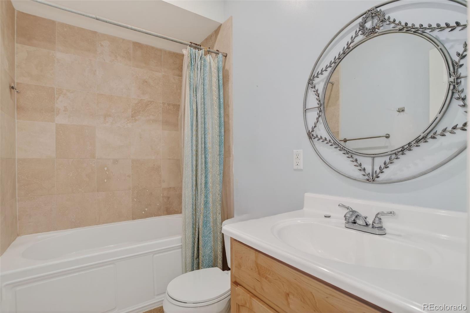 Bathroom with a tiled tub and shower, wood vanity, and ornate round mirror.