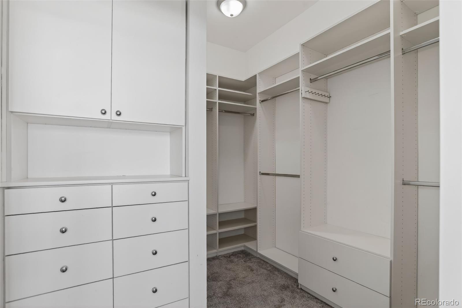 Walk-in closet with white built-in drawers, shelves, and hanging rods.