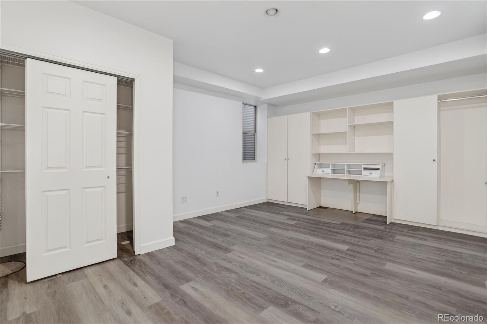 Unfurnished bedroom with built-in white desk and cabinets, open closets, and gray plank flooring.