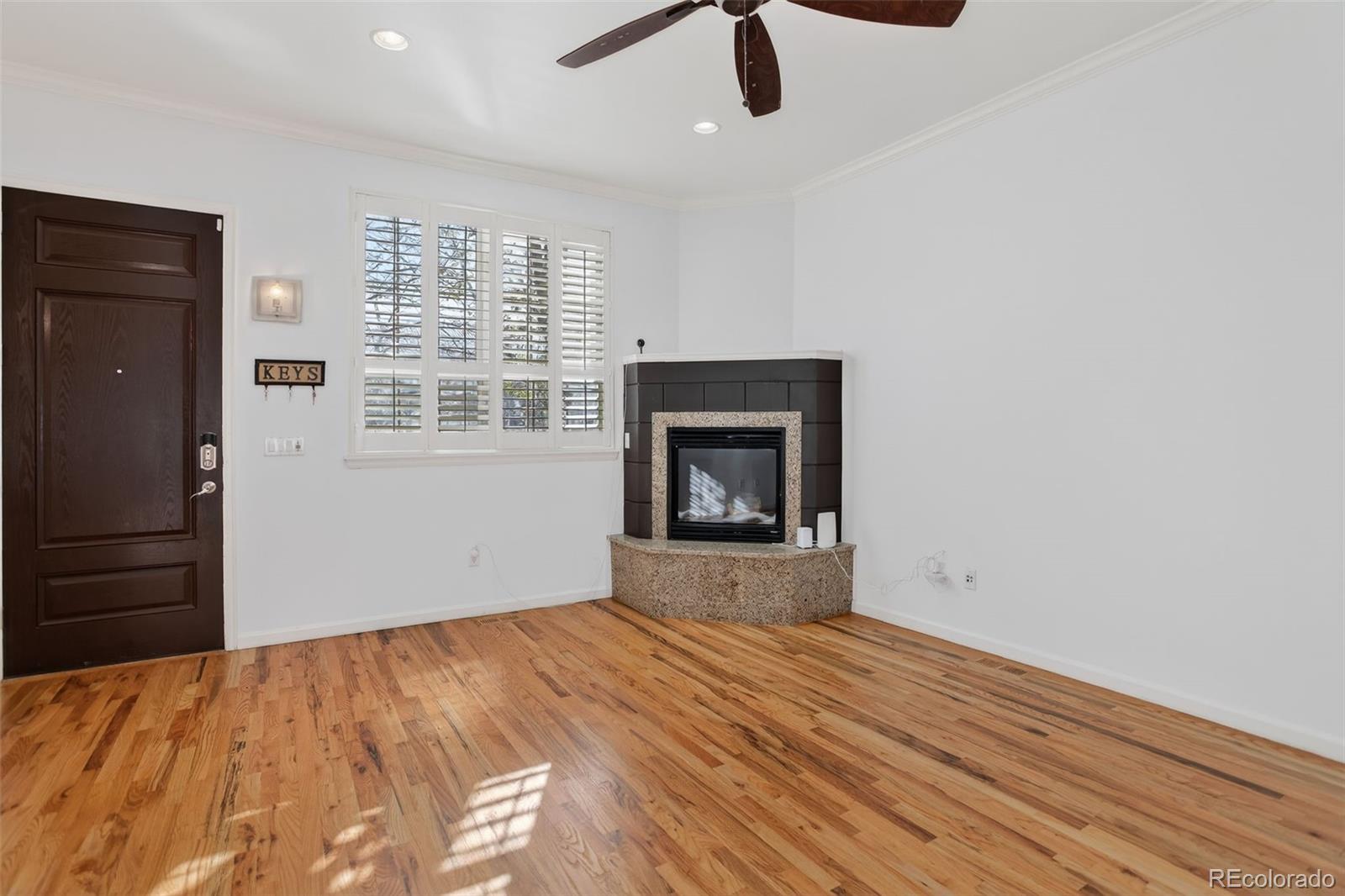 Vacant room with hardwood floors, a corner fireplace, and plantation-shuttered windows.