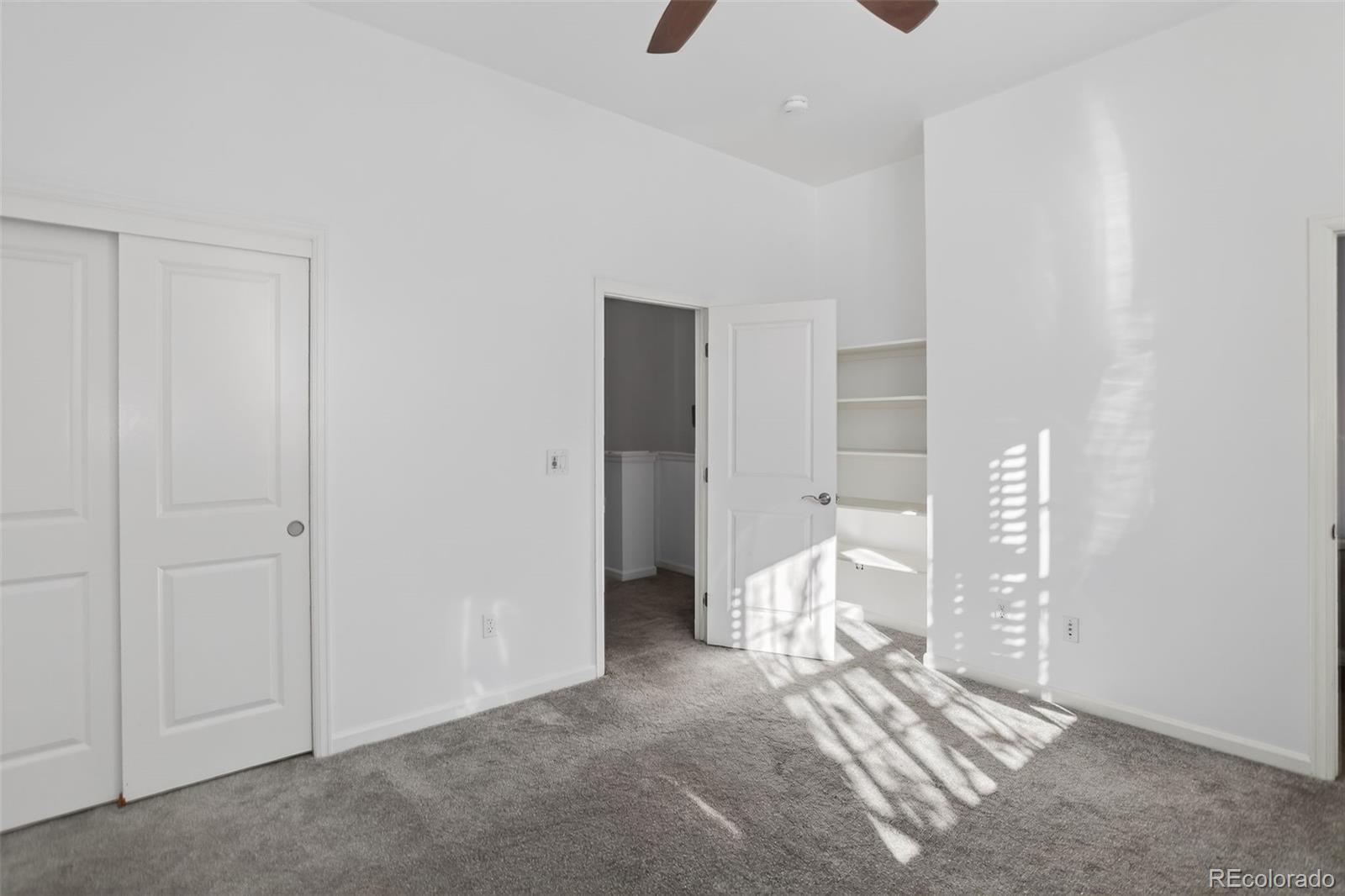 Empty bedroom with gray carpet, open closet shelving, and sunlight casting striped shadows across the floor.