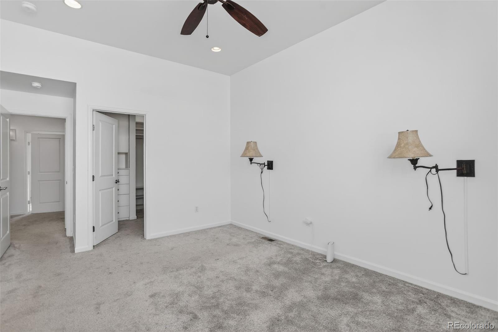 Unfurnished bedroom with gray carpet, a ceiling fan, and wall sconces beside an open closet.