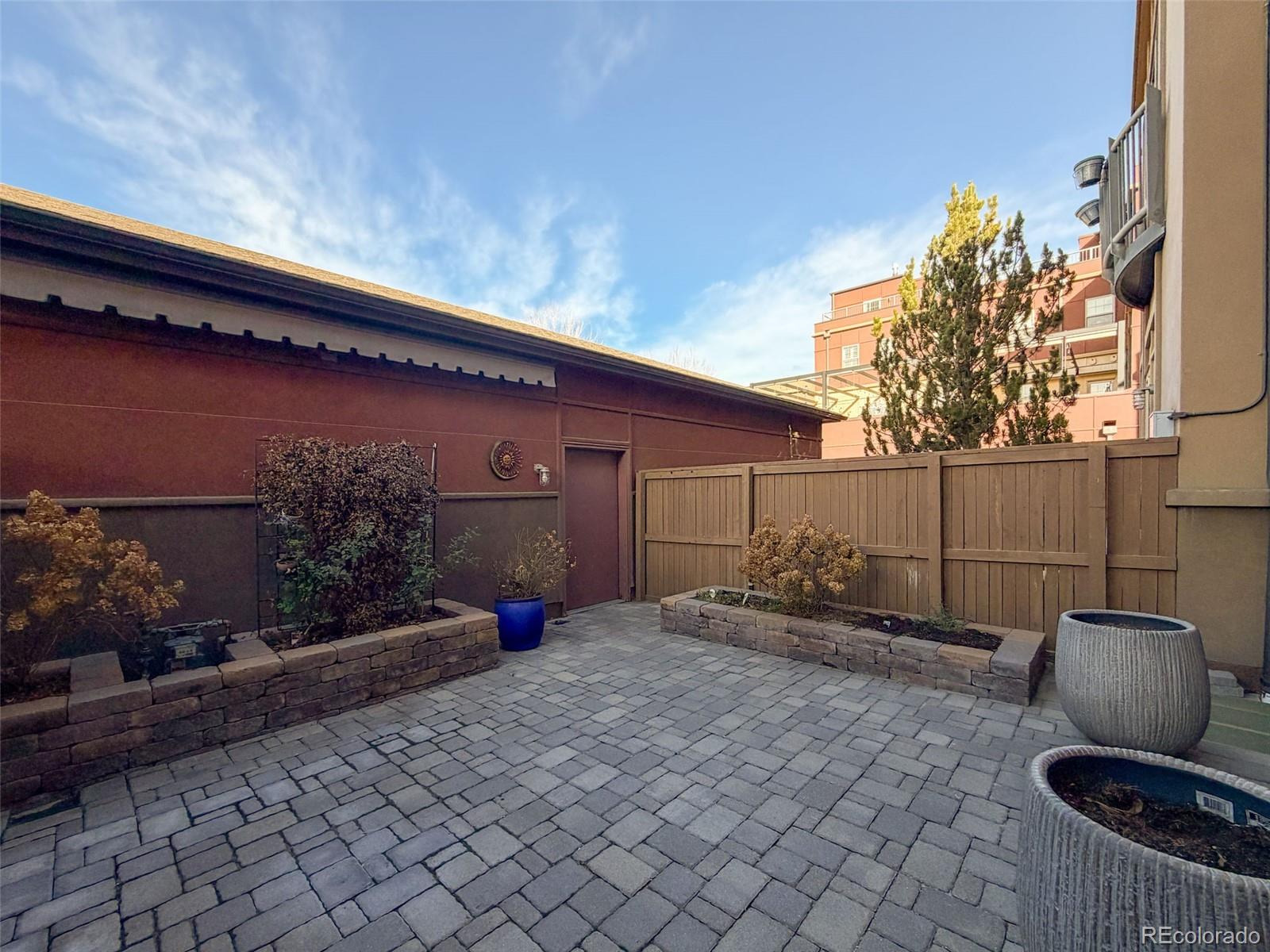 Private stone-paved patio with wooden privacy fence, raised planters, and potted plants.