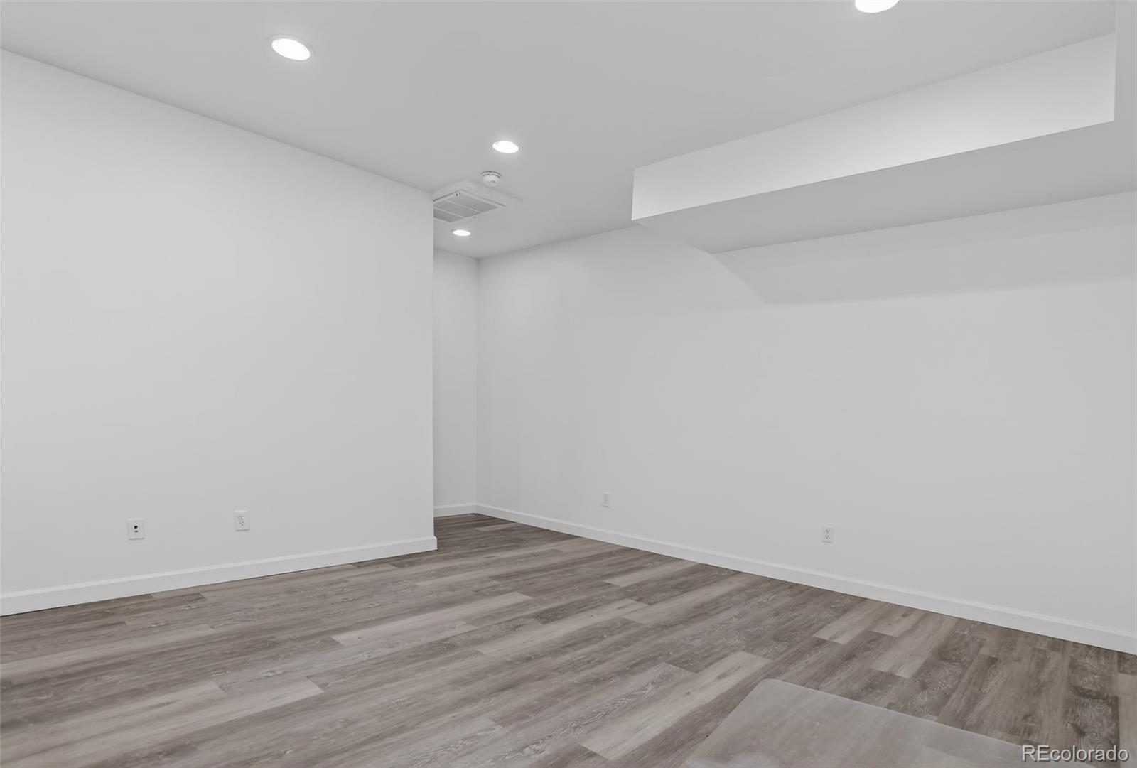 Empty room with gray plank flooring, white walls, and recessed ceiling lights.