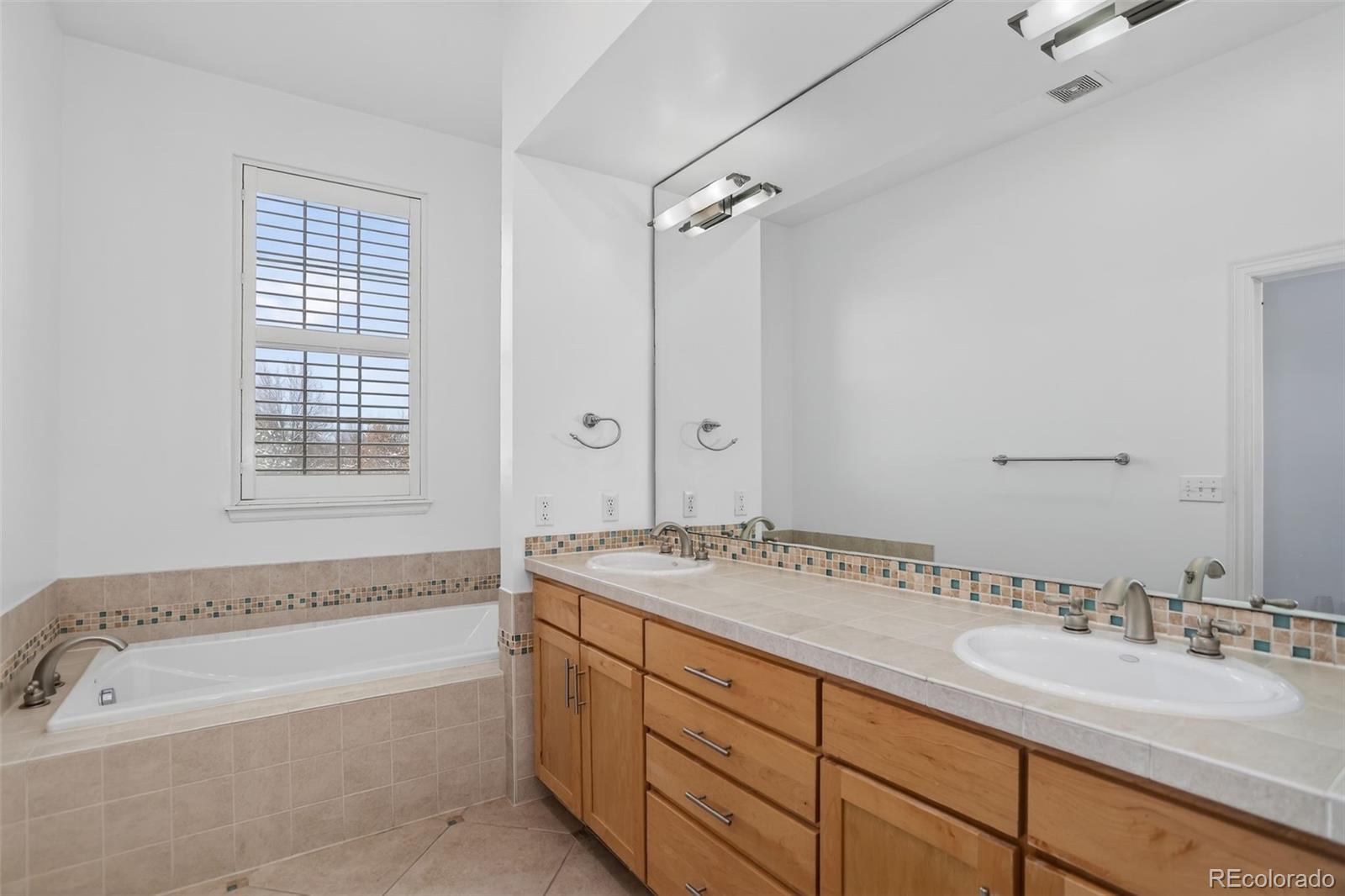 Bathroom with a built-in tub beneath a window and a long double-sink vanity with wood cabinets.