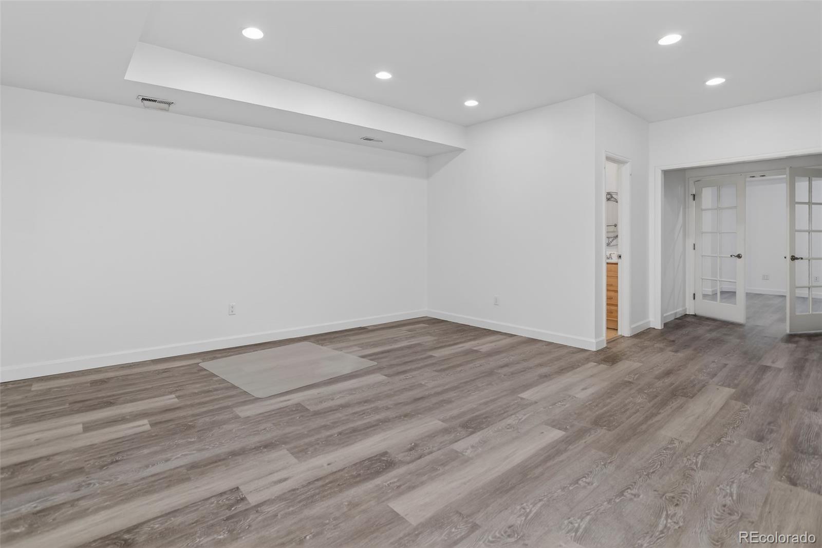 Empty interior room with gray plank flooring, recessed lights, and French doors.