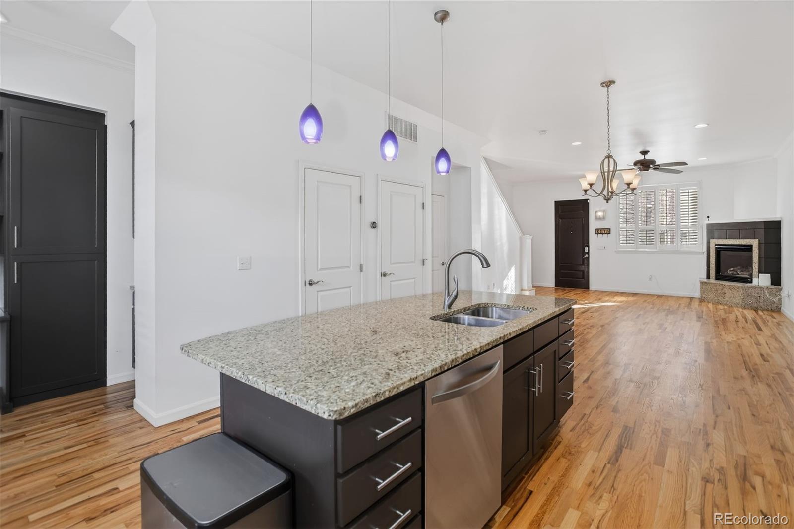 Open-plan kitchen with granite island and purple pendant lights opening to a hardwood-floored living area.