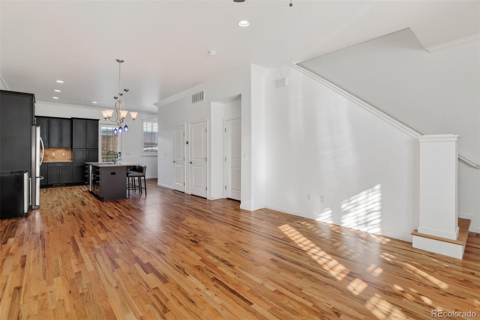 Open kitchen and living area with dark cabinets, an island, hardwood floors, and a staircase.