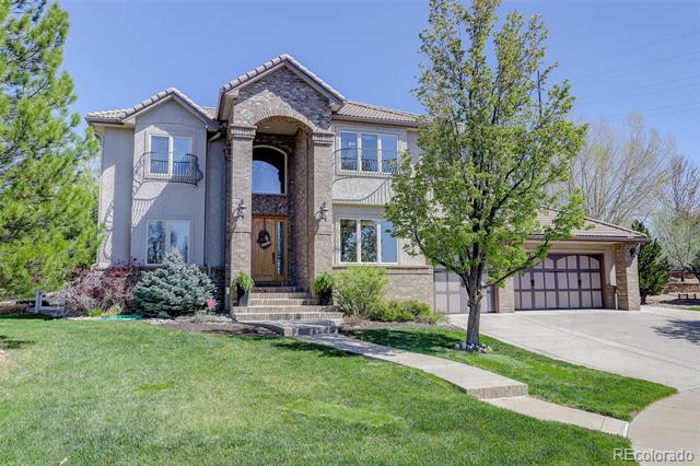 Two-story stone and stucco house with an arched entry and attached garage, framed by mature trees.