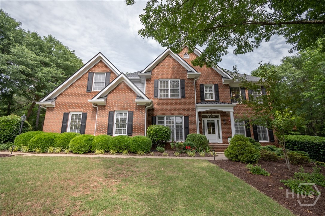 Two-story red-brick house with multiple gables, dark shutters, and landscaped front lawn.