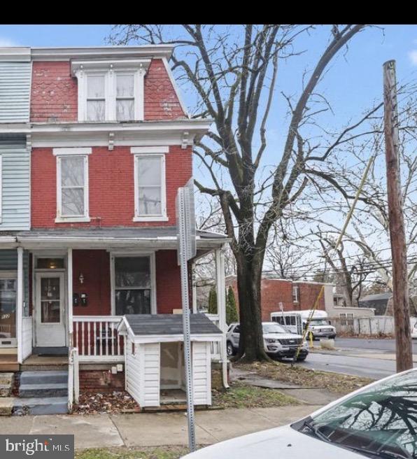 Red-brick home with white trim and a small covered front porch beside a leafless street tree.
