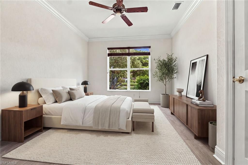 Staged bedroom with a large white bed, wood furnishings, and a window overlooking greenery.