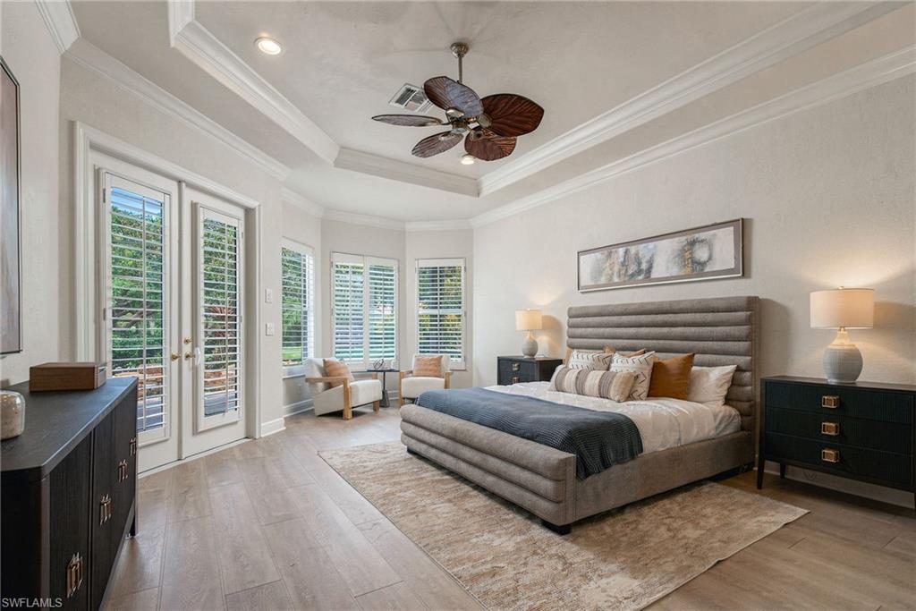 Primary bedroom with a tray ceiling, upholstered bed, and plantation shutters on tall windows and French doors.