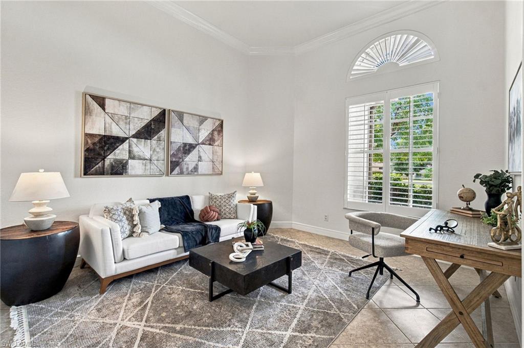 Staged living room with a white sofa, geometric wall art, and a desk beside shuttered windows.